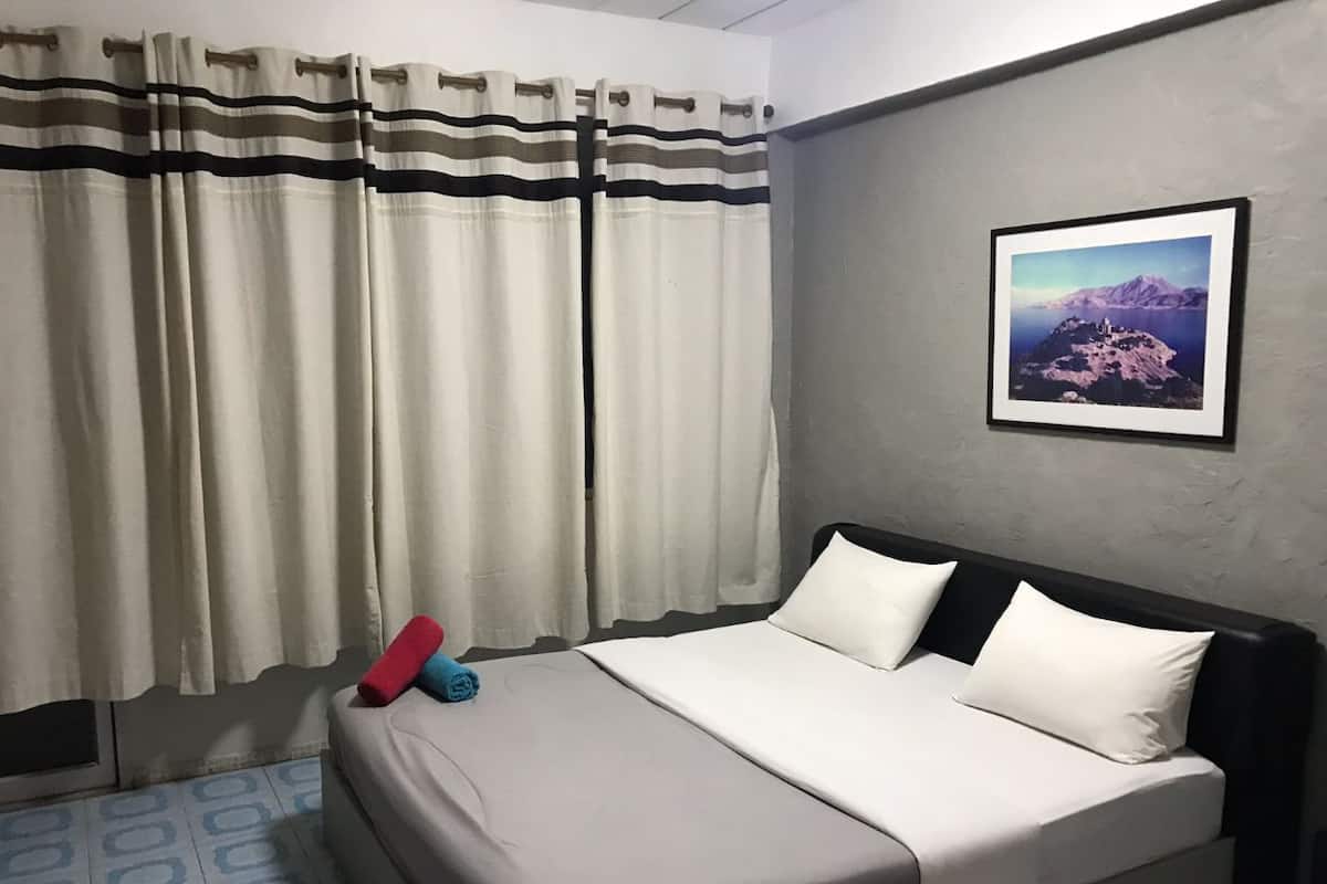 A hotel room with a bed, curtains, a pillow, a wall-mounted picture, and a patterned floor.