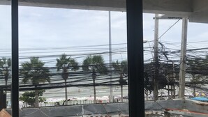A view through a window with numerous power lines and poles, with a beach and umbrellas visible outside. - Seaview (Pattaya)