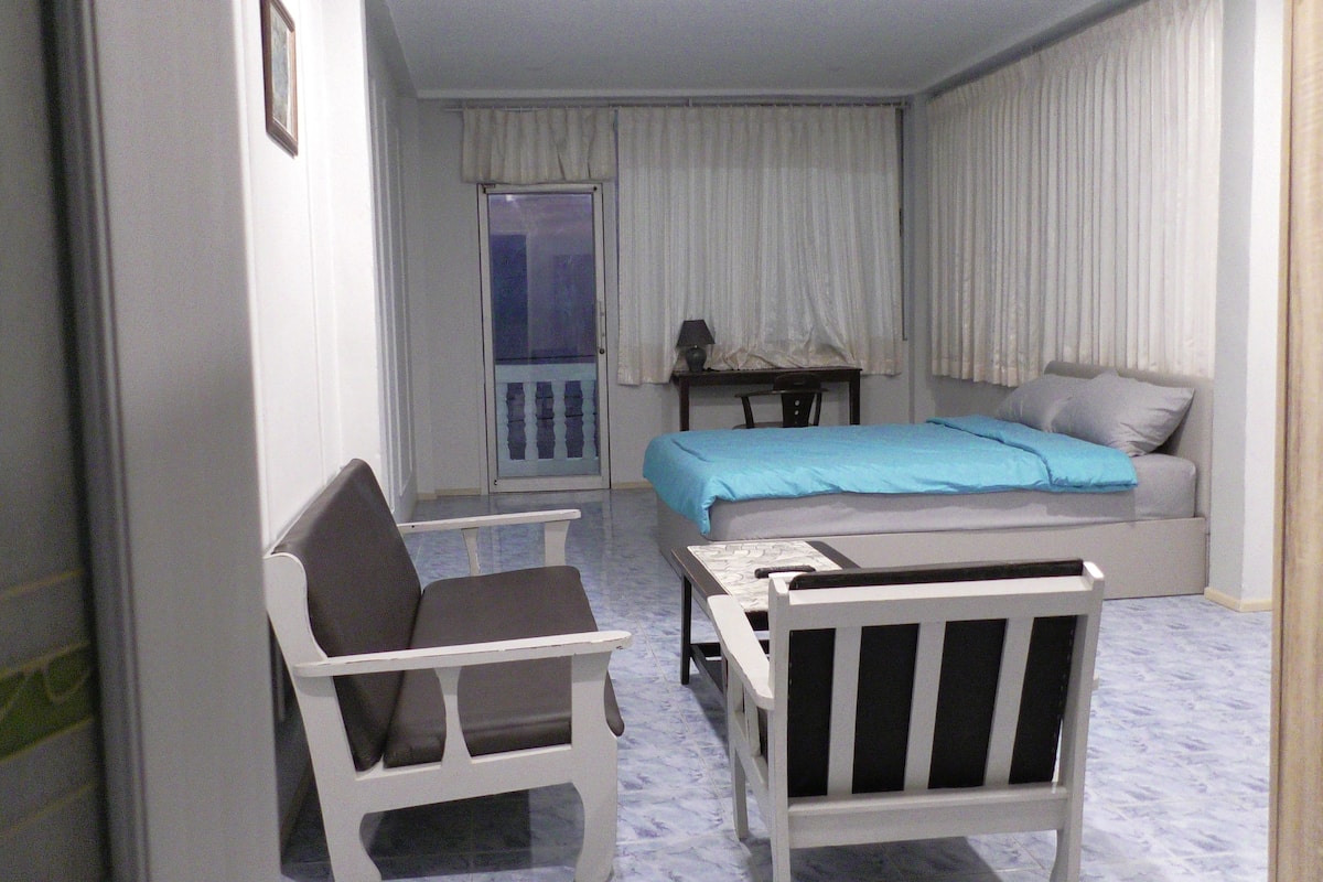 A small, compact hotel room with a bed, a chair, a small table, and a window with curtains.