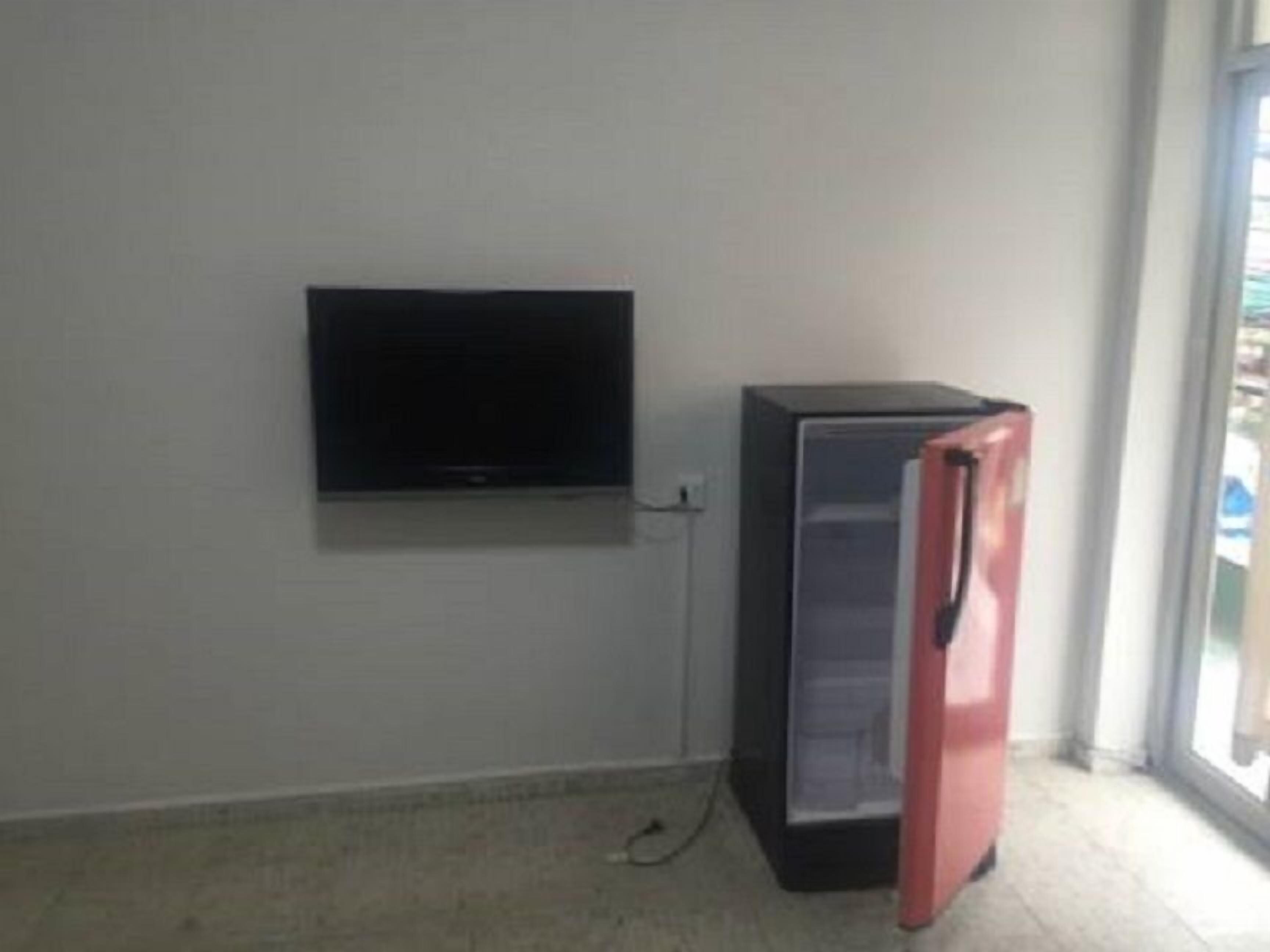 Huoneessa on seinälle asennettu televisio ja jääkaappi nurkassa.