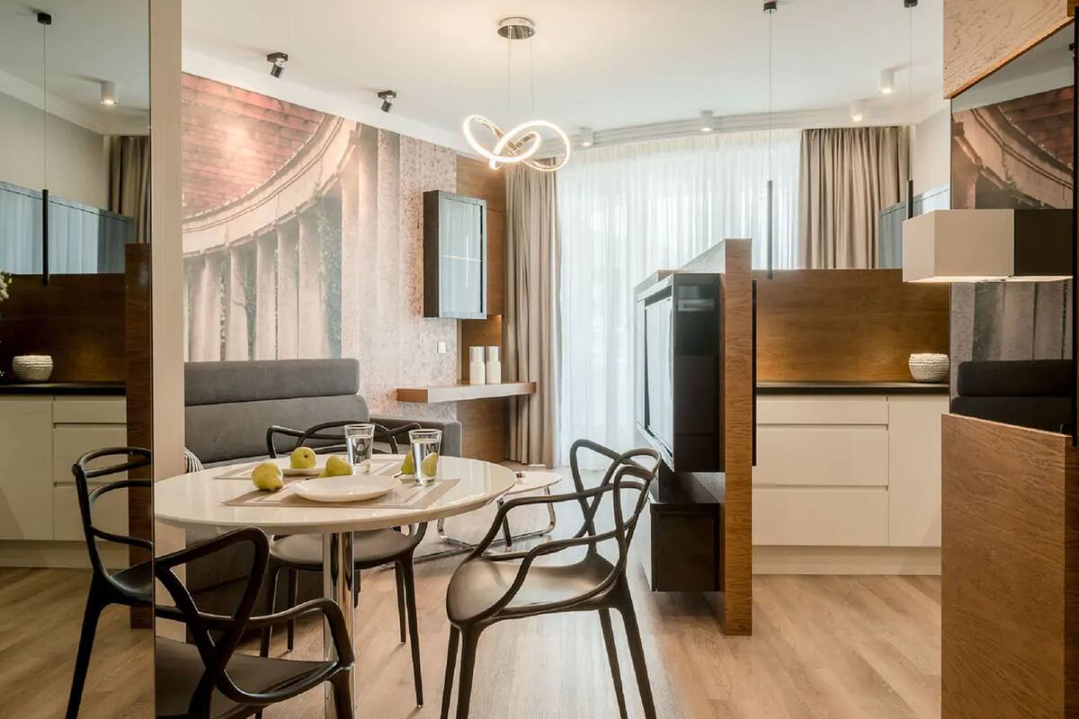 Une cuisine moderne avec un coin repas, comprenant une table ronde, des chaises et une grande fenêtre agrémentée de rideaux.