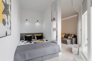 A modern bedroom with a bed, bedside tables, a grey sofa, and a brick wall.