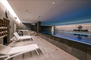 A modern hotel lobby with lounge chairs, a reception desk, and a large wall-mounted sign reading "HOLMES PLACE."