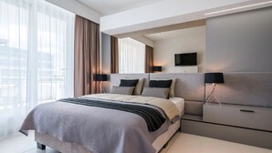 Ein modernes Hotelzimmer mit einem großen Bett, zwei Nachttischen, einem Flachbildfernseher und einem großen Fenster mit Vorhängen.