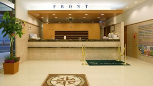 Un espace d’accueil d’hôtel avec une enseigne indiquant « RÉCEPTION », une horloge, une plante et un tapis orné d’un motif de boussole.