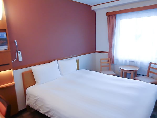 Une chambre d’hôtel avec un grand lit, une petite table, deux chaises et une fenêtre avec des rideaux.