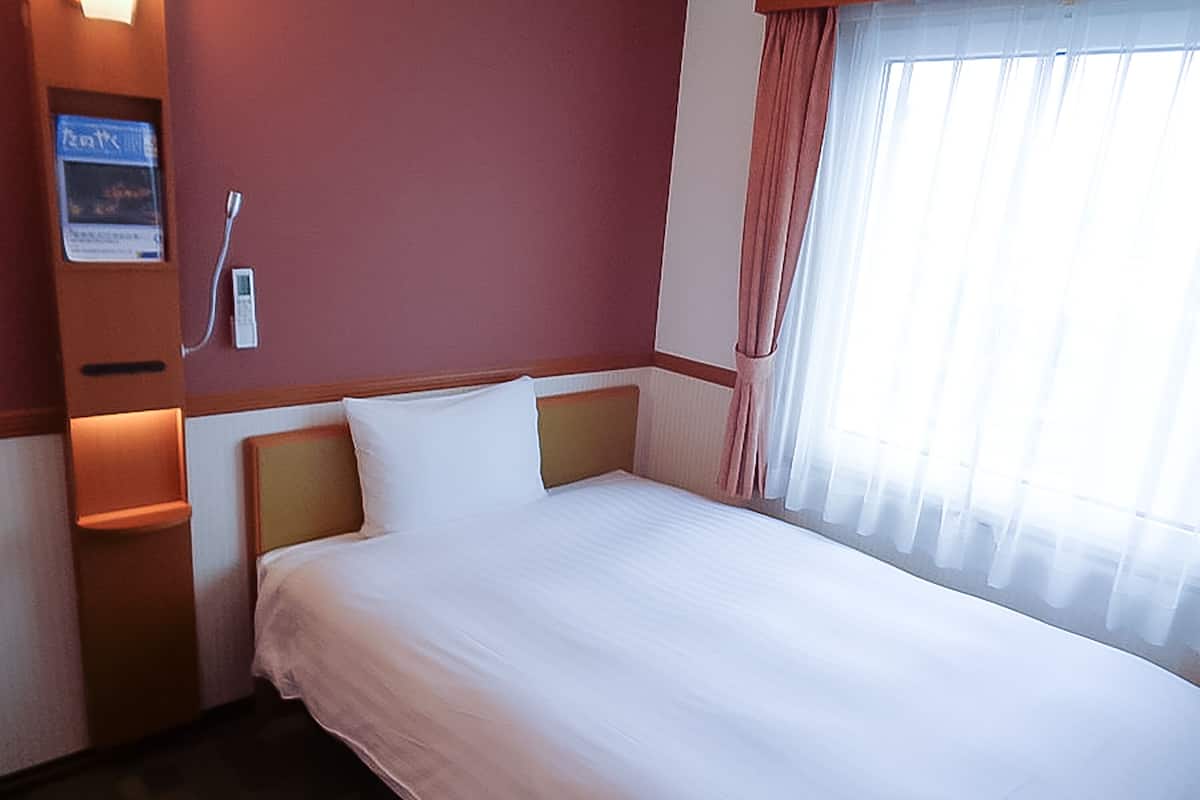 A hotel room with a large bed, a nightstand, a wall-mounted TV, and a window with curtains.