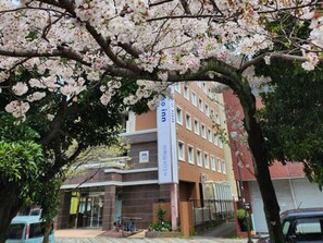 Een hotel met een bord, een meerhoog gebouw en een boom met roze bloesems op de voorgrond.