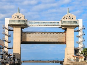 Un puente de hormigón grande con dos torres, un paso para peatones y vistas al agua y montañas distantes.