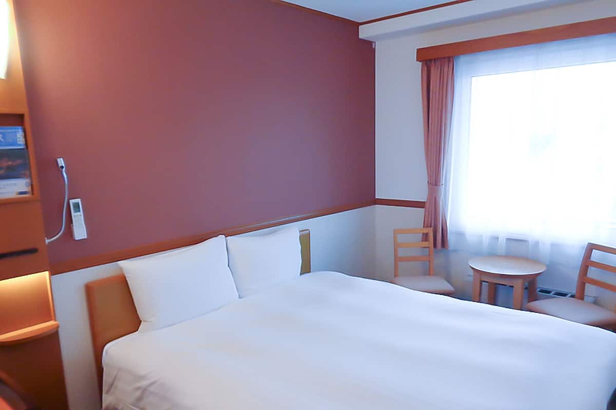 A hotel room with a large bed, a small table, two chairs, and a window with curtains.