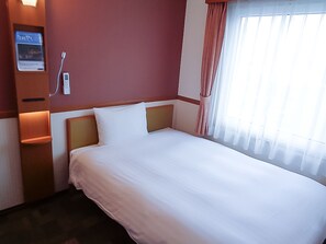 Une chambre d’hôtel avec un grand lit, une table de chevet, un téléviseur fixé au mur et une fenêtre avec des rideaux.