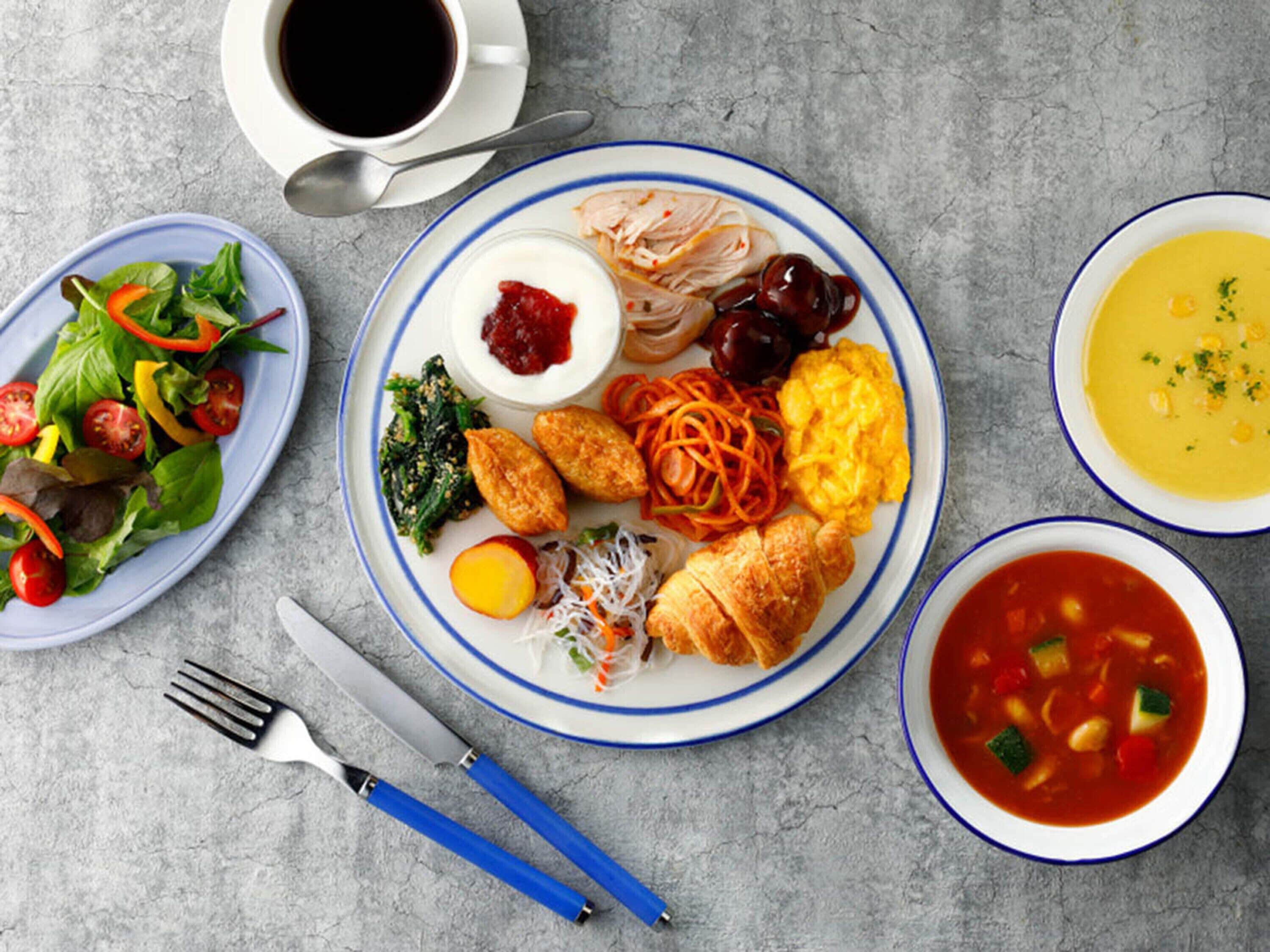 Ein reichhaltiges Frühstücksbuffet mit verschiedenen Speisen, darunter Rührei, ein Croissant, ein Salat und eine Schüssel Suppe.