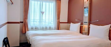 Habitación de hotel con una cama grande, una mesita de noche, una silla, una ventana con cortinas y una lámpara de pared.