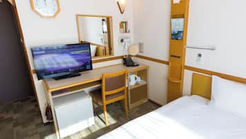 A hotel room with a bed, a desk with a computer, a chair, a small refrigerator, a clock, and a mirror.