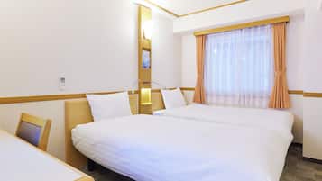 Habitación de hotel con dos camas, un escritorio, una mesita de noche, una lámpara, una ventana con cortinas y un teléfono en la pared.