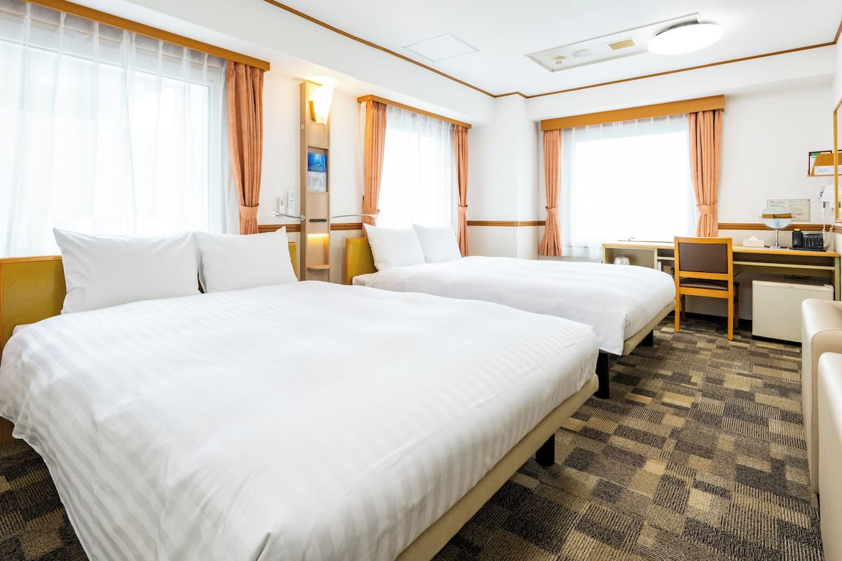 A hotel room with two beds, a desk, a chair, and a small kitchenette.