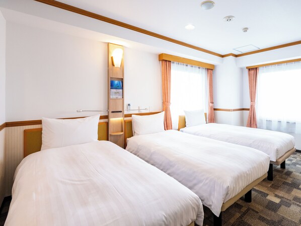 A hotel room with two beds, a wooden headboard, a nightstand, a wall-mounted lamp, and a window with curtains.