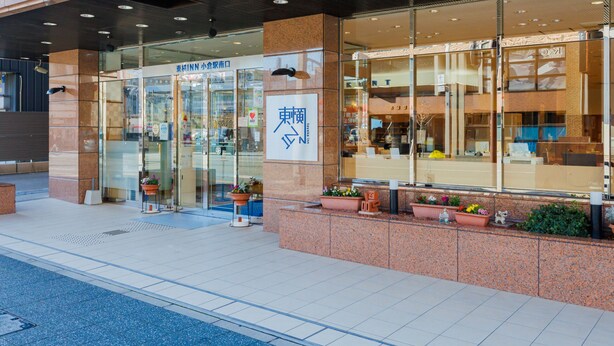 A building with a glass facade, a sign with Japanese characters, and potted plants at the entrance. - Toyoko Inn Kokura Station Minami (Kitakyushu)