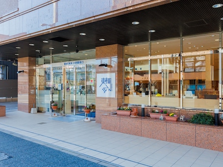 A building with a glass facade, a sign with Japanese characters, and potted plants at the entrance.