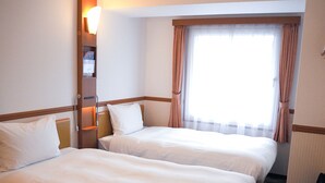 A hotel room with two beds, a nightstand, a lamp, and a window with curtains. - Toyoko Inn Kokura Station Minami (Kitakyushu)