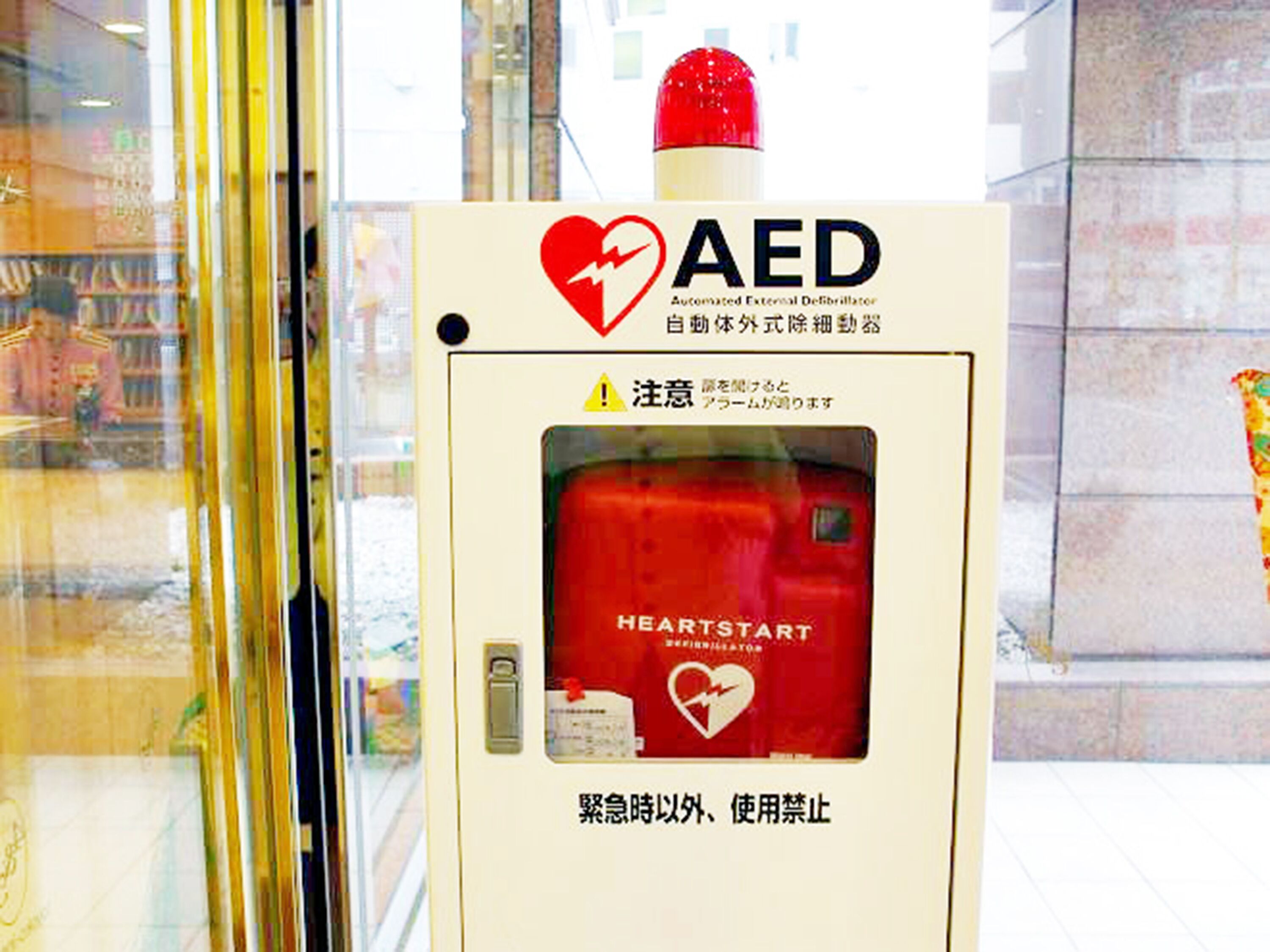 An AED device with a red heart symbol and text in multiple languages, including English and Japanese.