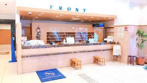 A hotel reception area with a marble counter, a 'Front' sign, a reception desk, a small wooden stool, a blue mat with the hotel logo, and a potted plant. - Toyoko Inn Osaka Hankyu Juso Station Nishi (Osaka)