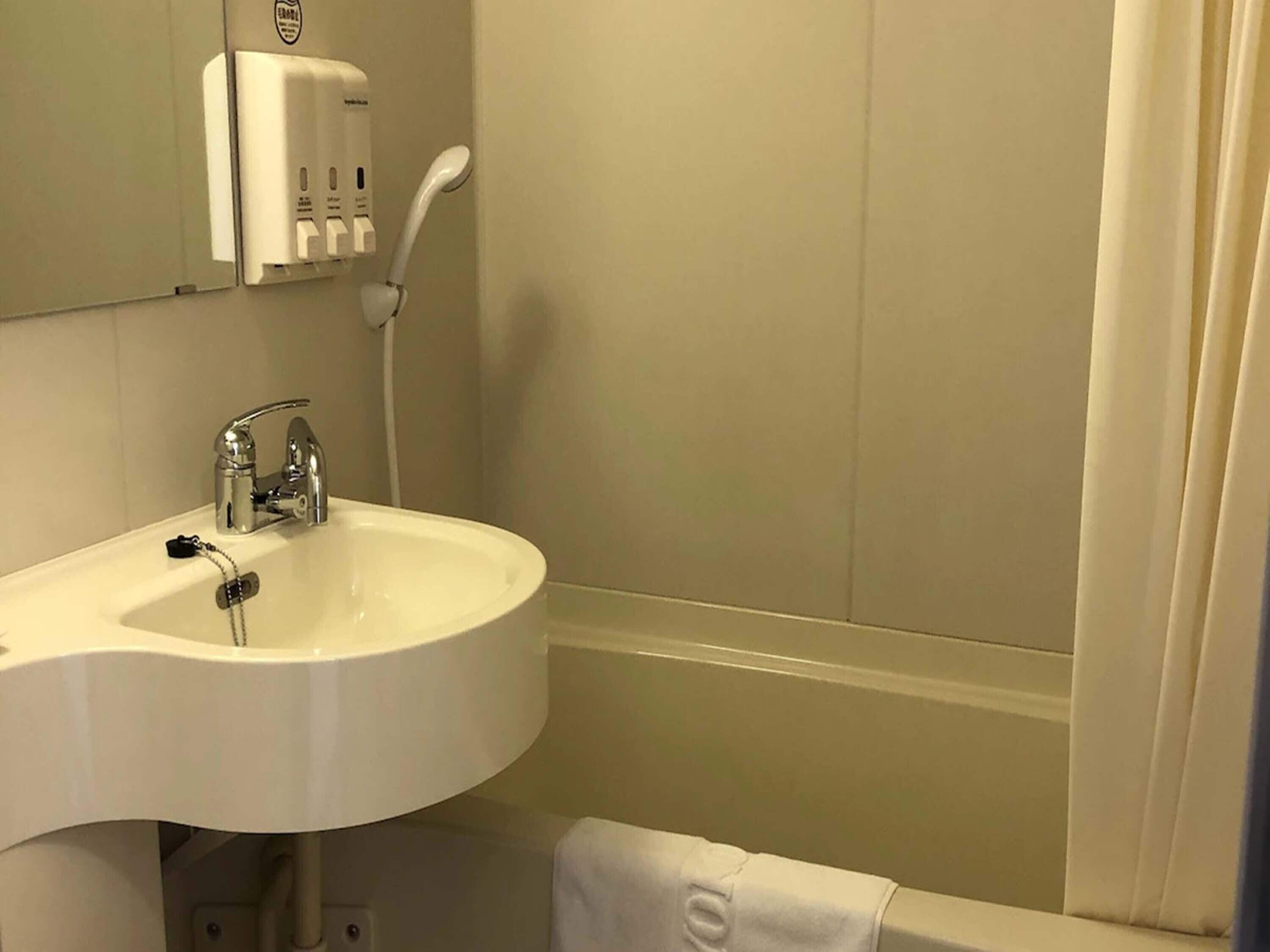 A bathroom with a white sink, a mirror, and a hand dryer.