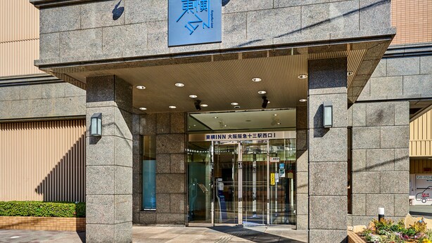 A building entrance with a stone facade, a blue sign with Chinese characters, and a glass door entrance. - Toyoko Inn Osaka Hankyu Juso Station Nishi (Osaka)