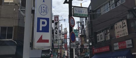 Une vue de rue avec un panneau de signalisation indiquant un parking, un bâtiment orné d’un symbole « P », et divers panneaux en langue étrangère.
