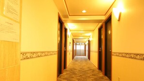 A hotel hallway with carpeted floors, wooden doors, and wall-mounted light fixtures.