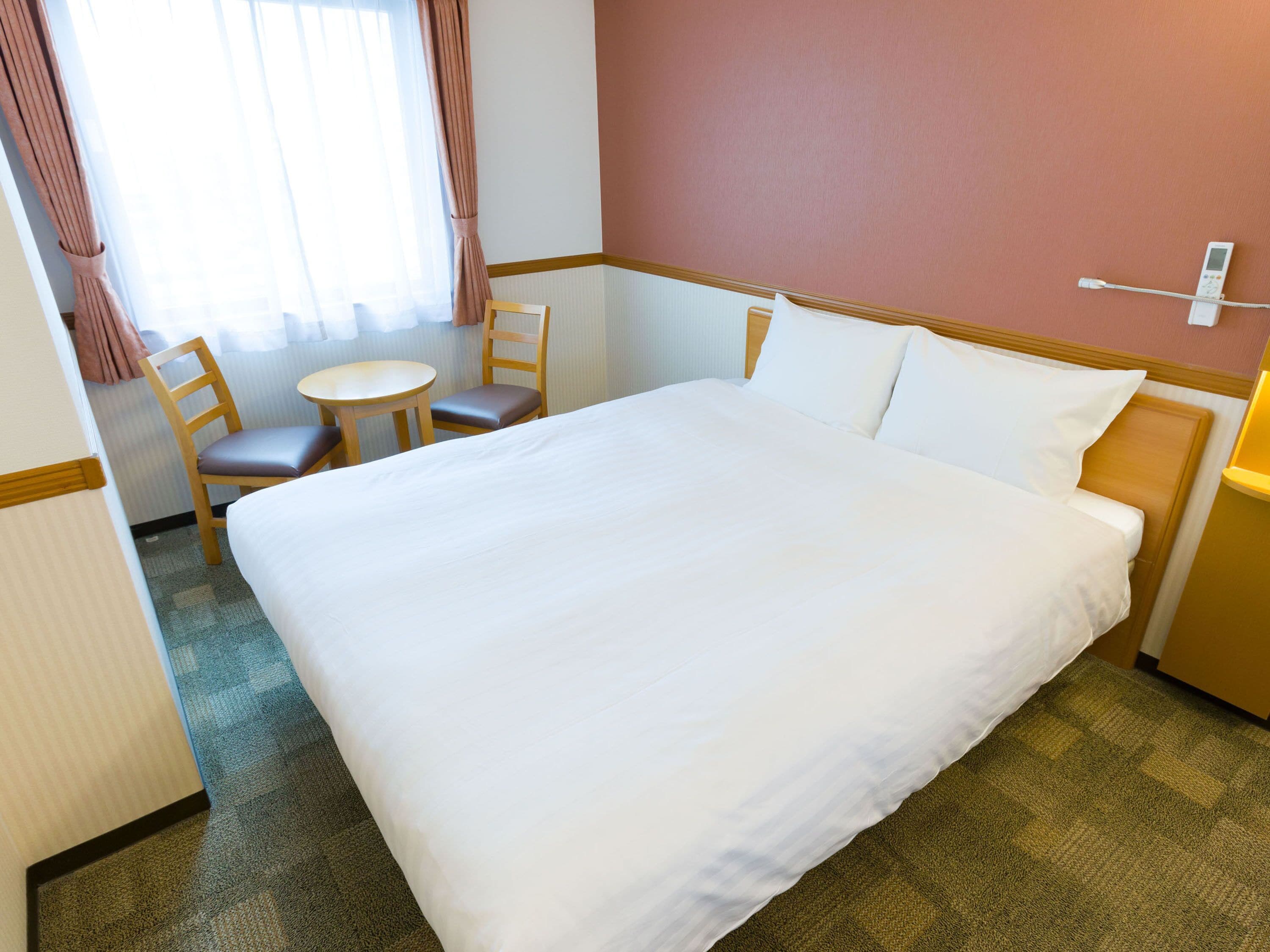 A hotel room with a large bed, a small round table, two chairs, and a bedside table with a lamp.