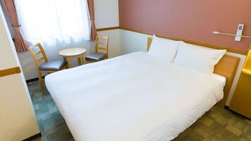A hotel room with a large bed, a small round table, two chairs, and a bedside table with a lamp.