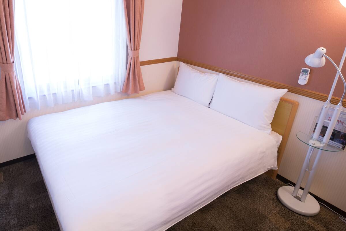 A neatly made bed in a hotel room with a bedside lamp and a control panel on the wall.