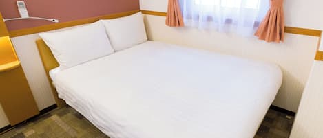 A hotel room with a neatly made bed, a bedside lamp, a telephone, and a window with curtains.