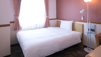 A hotel room with a bed, a bedside lamp, a window with curtains, and a wall-mounted telephone.