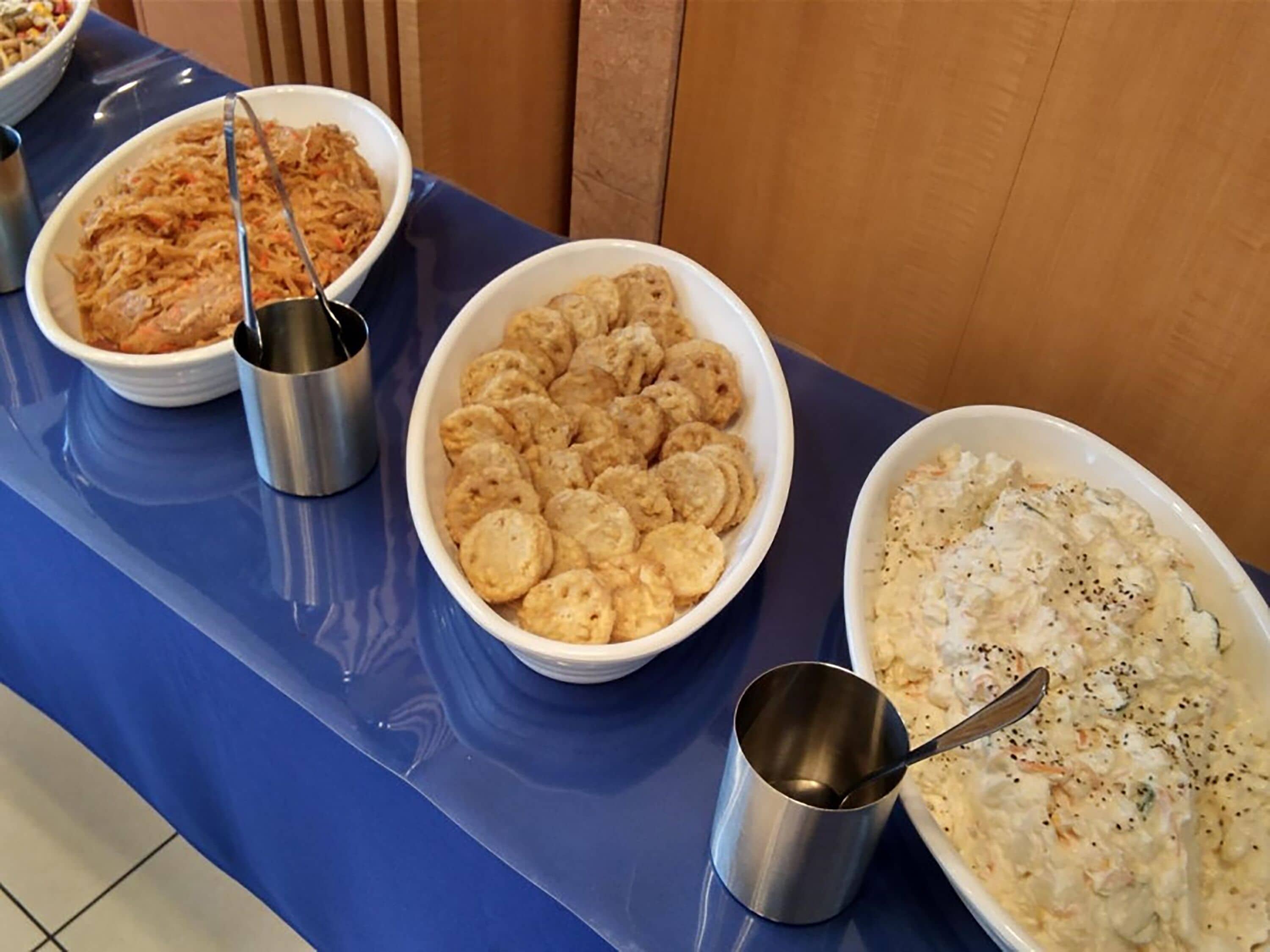 A table with three bowls of food, a metal cup, and a spoon.