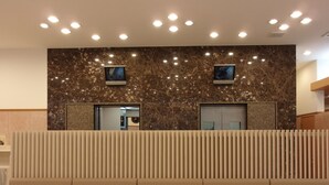 Un espace d’accueil moderne avec un mur en marbre, deux écrans, un coin salon avec des tables rondes et un plafond doté d’un éclairage encastré.