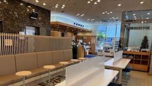 Un restaurant moderne doté d’un espace où l’on peut s’asseoir, avec de longues tables et des tabourets hauts, un comptoir où est affiché le menu, et un mur décoratif orné d’une horloge.