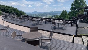 Une terrasse sur le toit, aménagée avec des tables et des chaises, offrant une vue sur les montagnes lointaines et le paysage urbain.