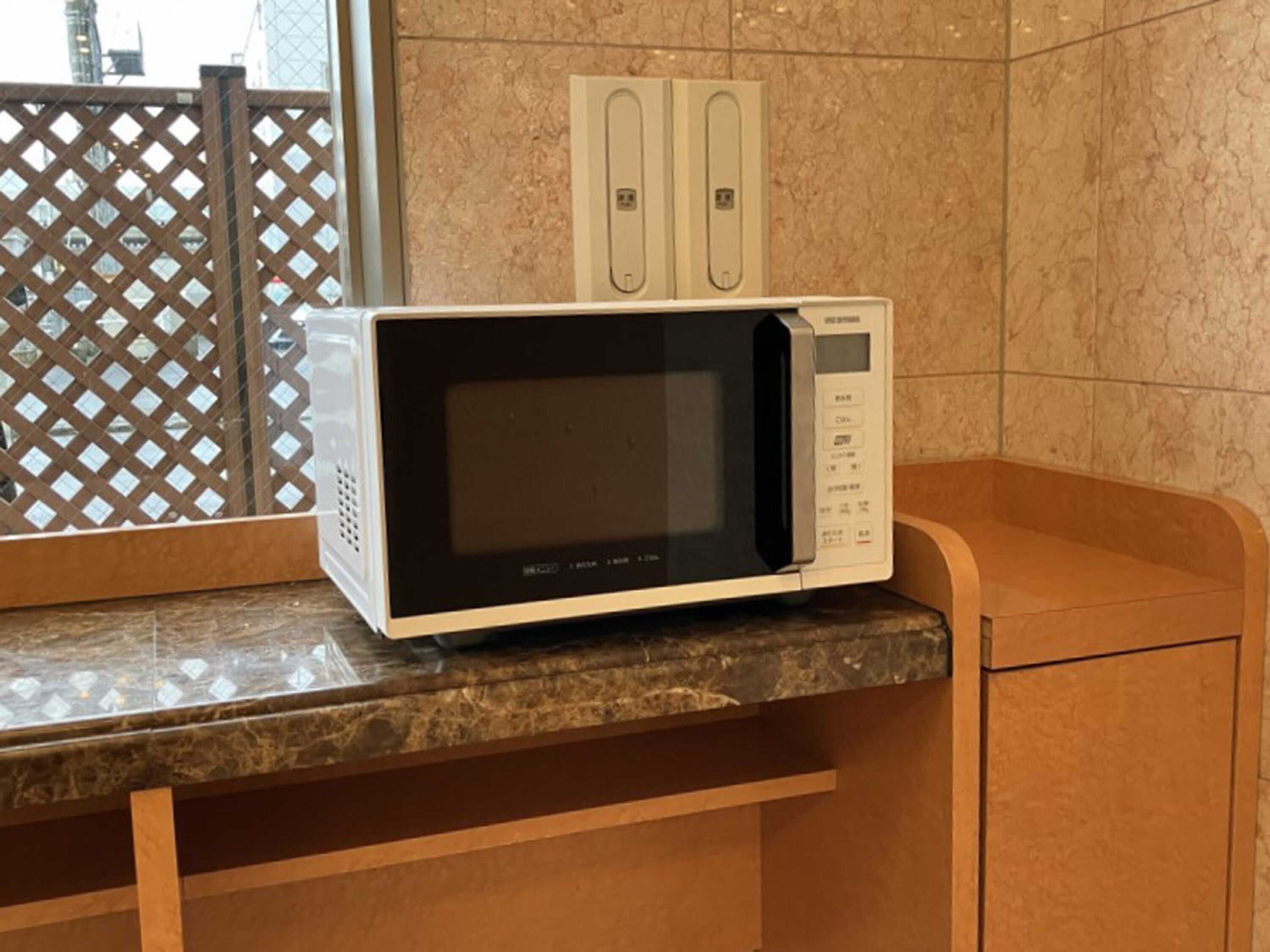 A microwave oven on a marble countertop in a kitchen area with a tiled backsplash and a wooden cabinet.
