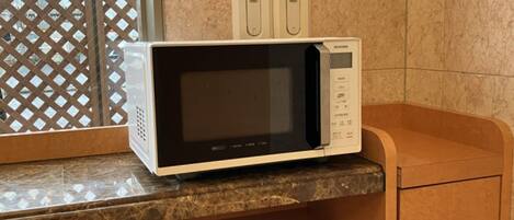 A microwave oven on a marble countertop in a kitchen area with a tiled backsplash and a wooden cabinet.
