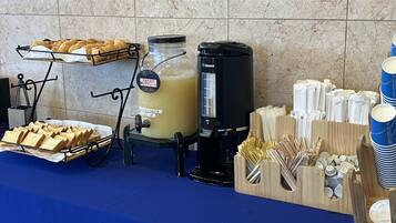 A buffet setup with bread, a beverage dispenser, and utensils.