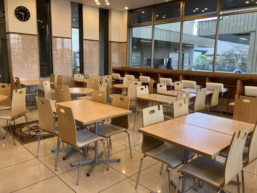 A modern dining area with multiple tables and chairs, large windows, and a clock on the wall.