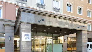 Ein Hotel mit steinverkleideter Fassade, Glastüren und einem Schild in einer Fremdsprache.