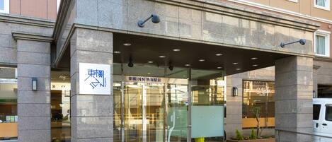 A hotel entrance with a stone facade, glass doors, and a sign in a foreign language.