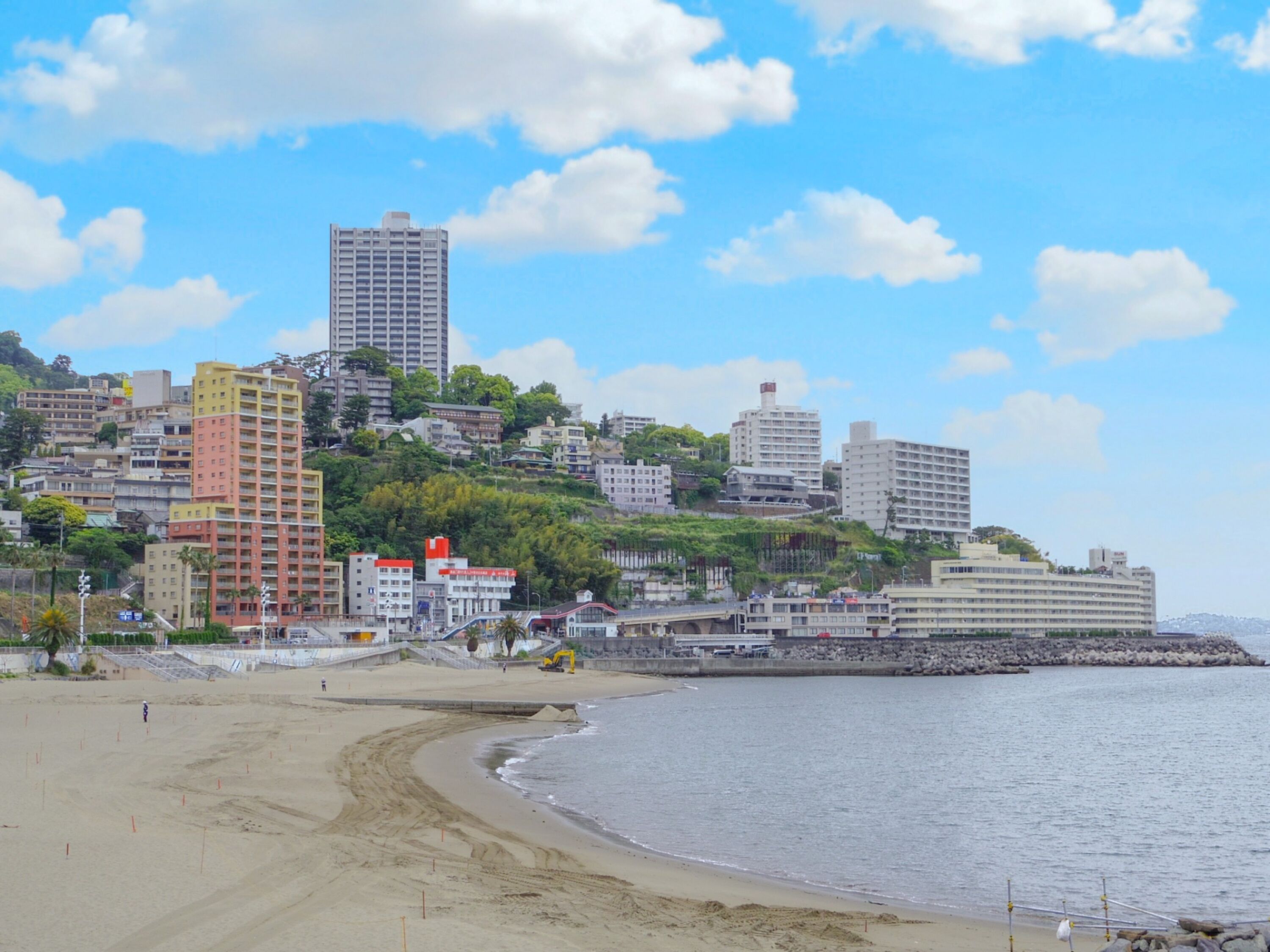 Un paisaje urbano costero con una playa, edificios altos y un litoral rocoso.
