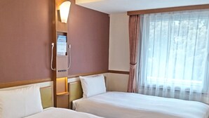 Ein Hotelzimmer mit zwei Betten, einem Fenster mit durchsichtigen Vorhängen und einer Wandleuchte.