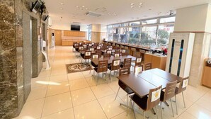 Un grand espace dédié à la salle à manger, avec plusieurs tables et chaises, un comptoir de cuisine et une grande fenêtre qui laisse entrer la lumière naturelle.