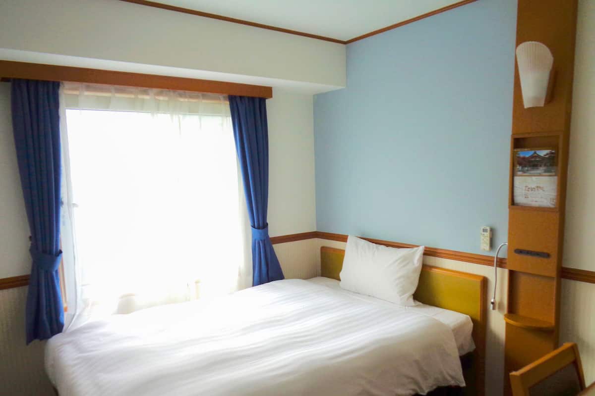 Hotelkamer met een bed, gordijnen, een nachtkastje en een telefoon aan de muur.