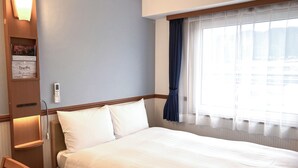 Une chambre d’hôtel avec un grand lit, une table de chevet, une chaise, un téléviseur fixé au mur et une fenêtre avec des rideaux.